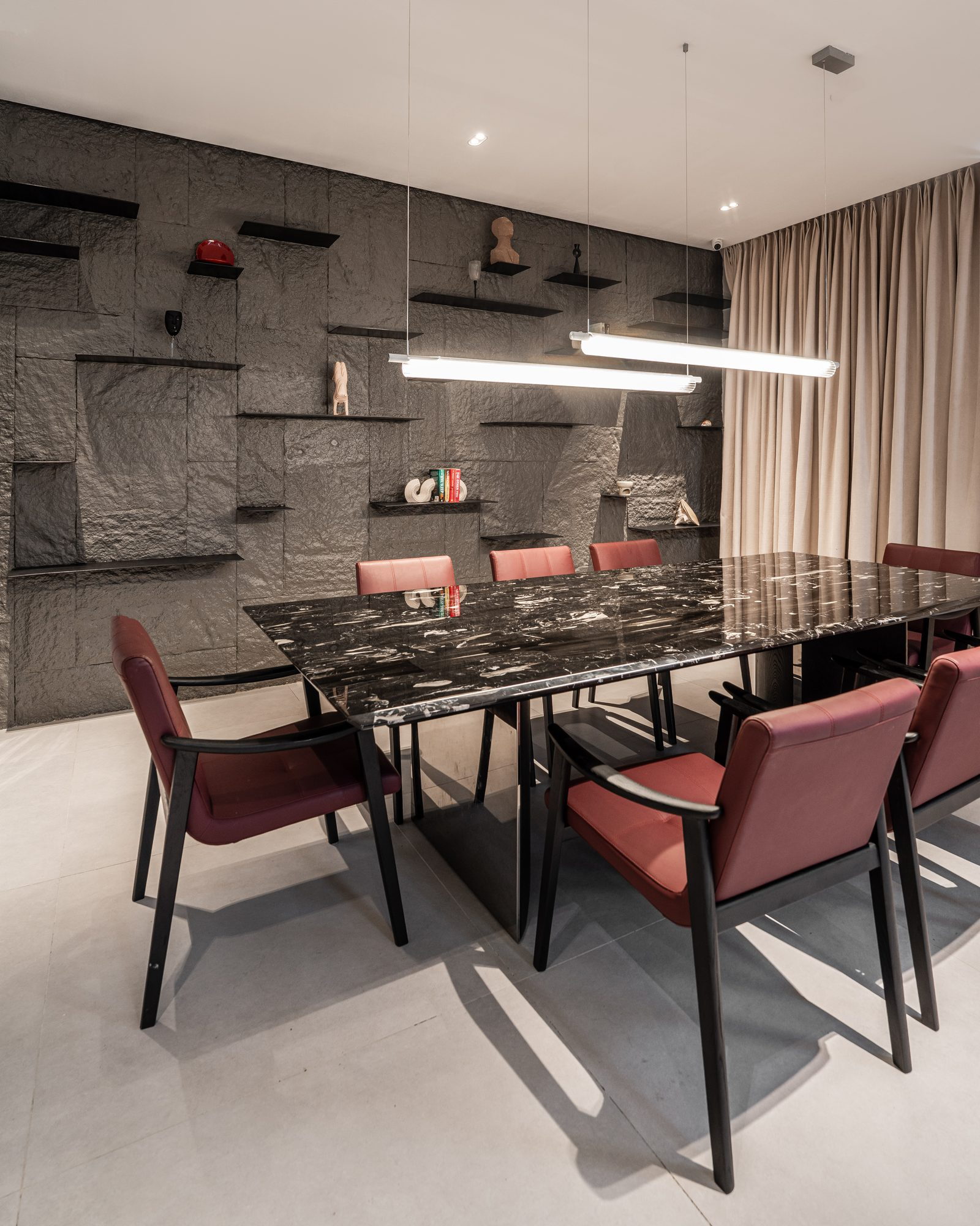 Dining room: a black marble table and oxblood leather chairs beneath a linear pendant, the wall of cleft slate behind