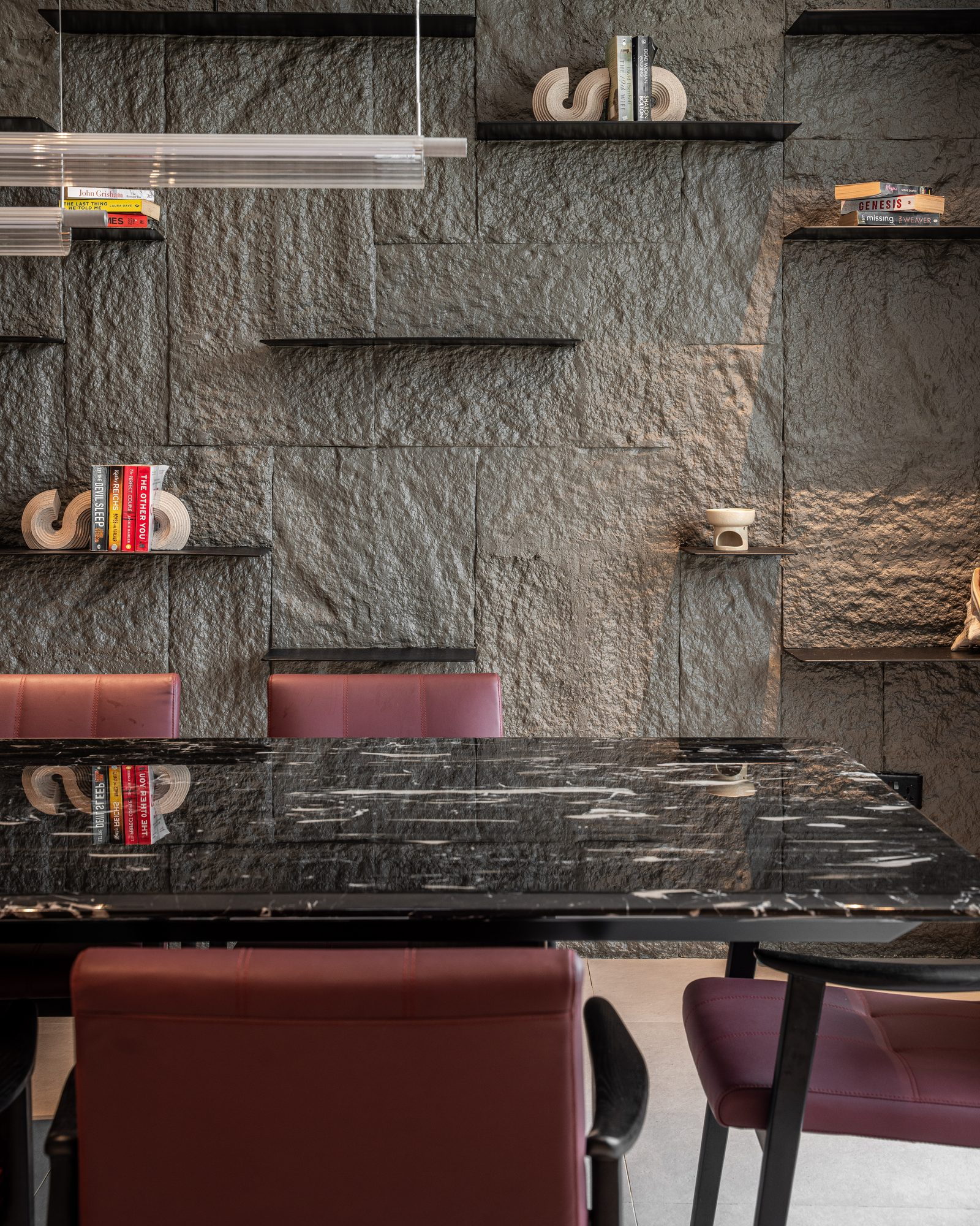 Dining table beneath a linear pendant, the slate wall beyond