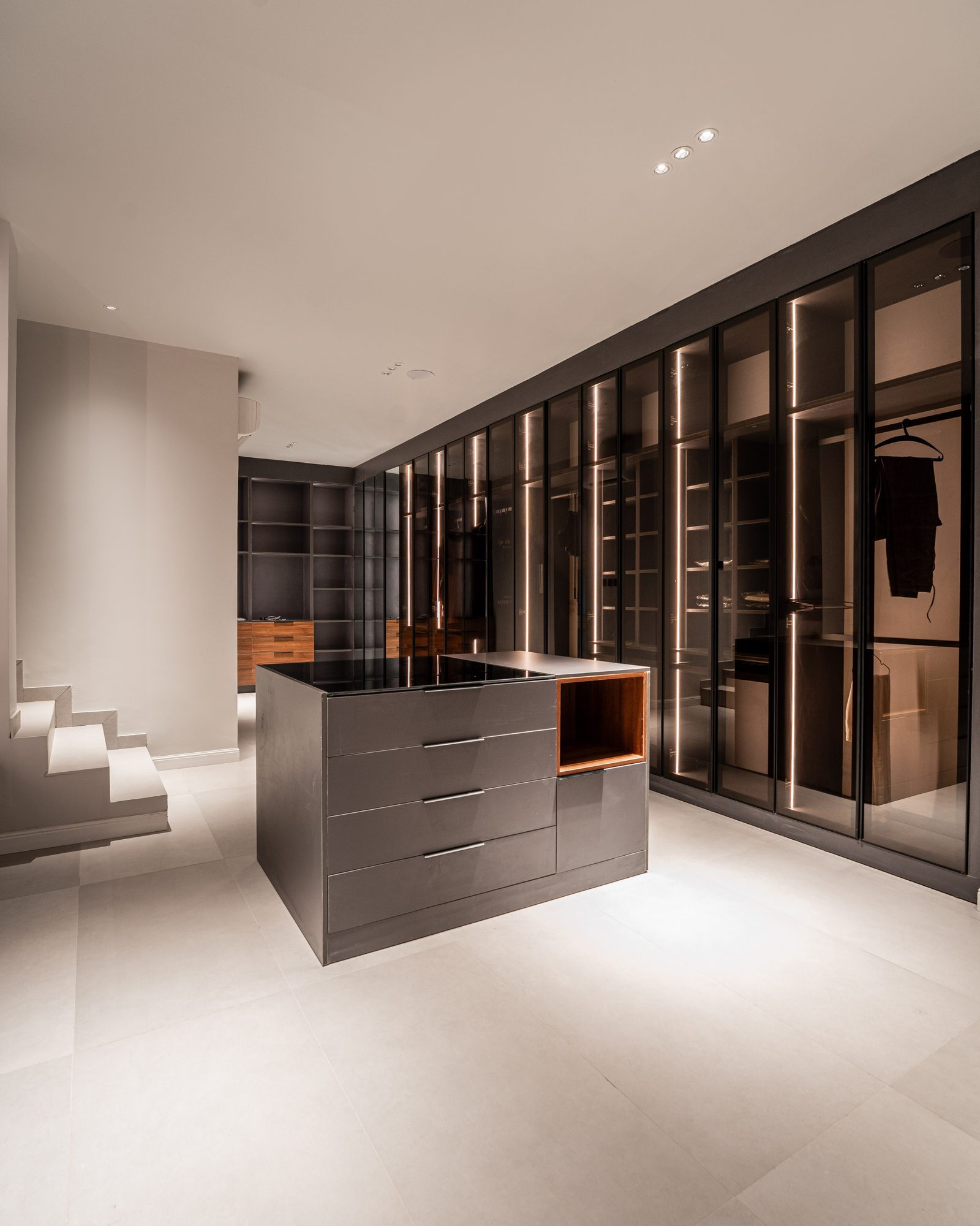 Dressing room: a dark island with timber drawers, wardrobes in back-lit glass