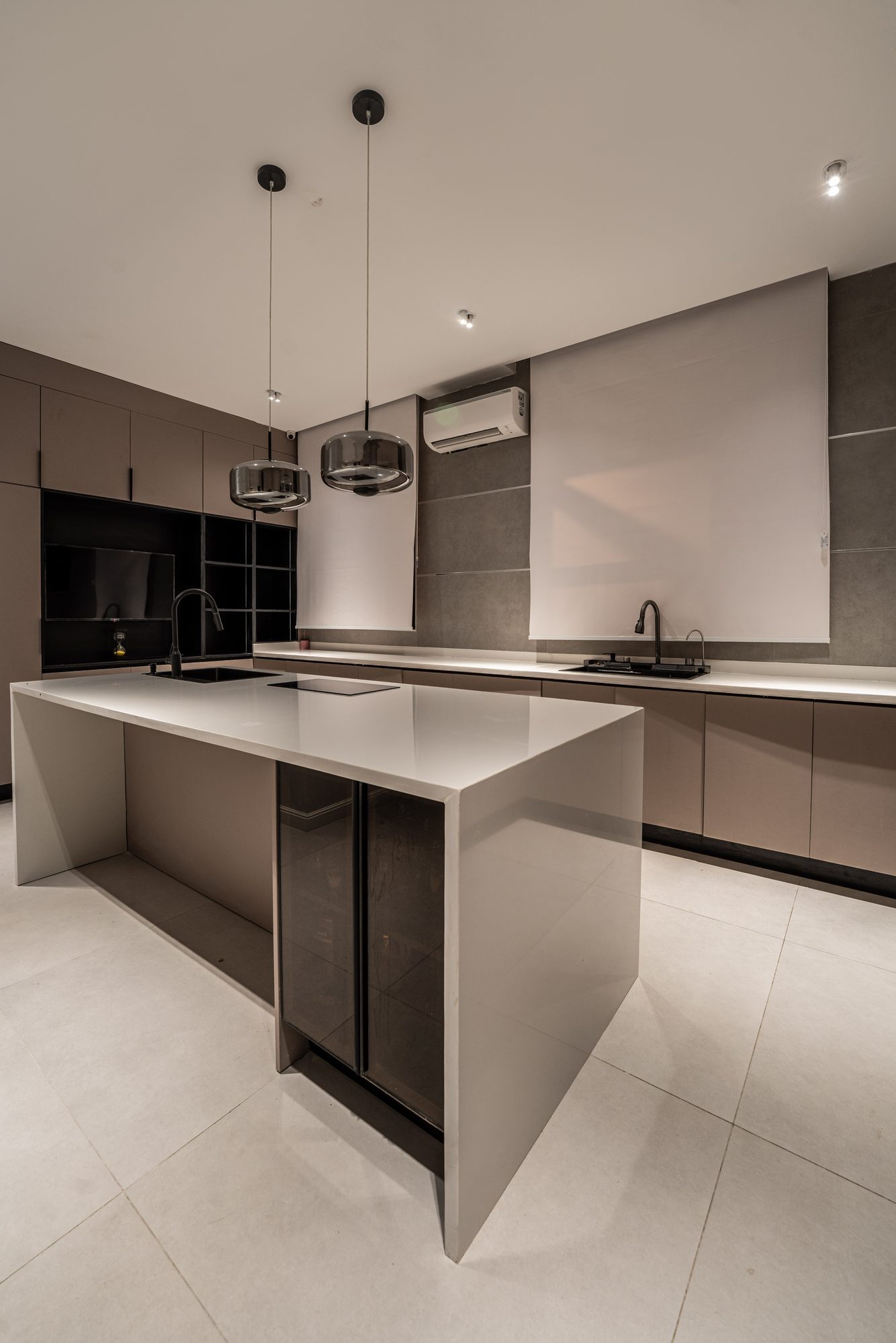 Kitchen: a taupe island with a waterfall stone top under two smoked-glass pendants