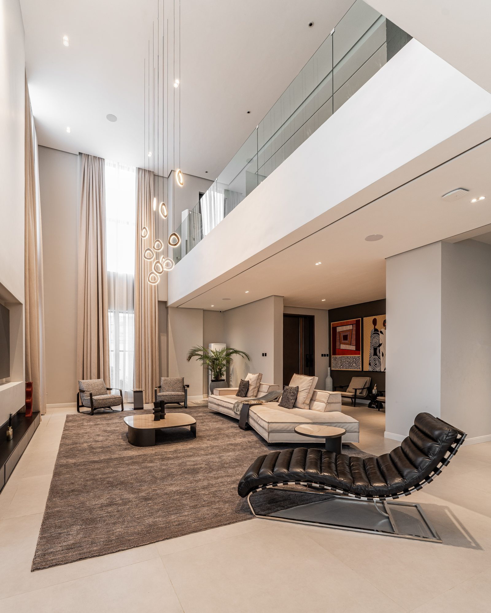 Double-height living room: a black leather chaise on a taupe rug beneath a cascade of ring pendants