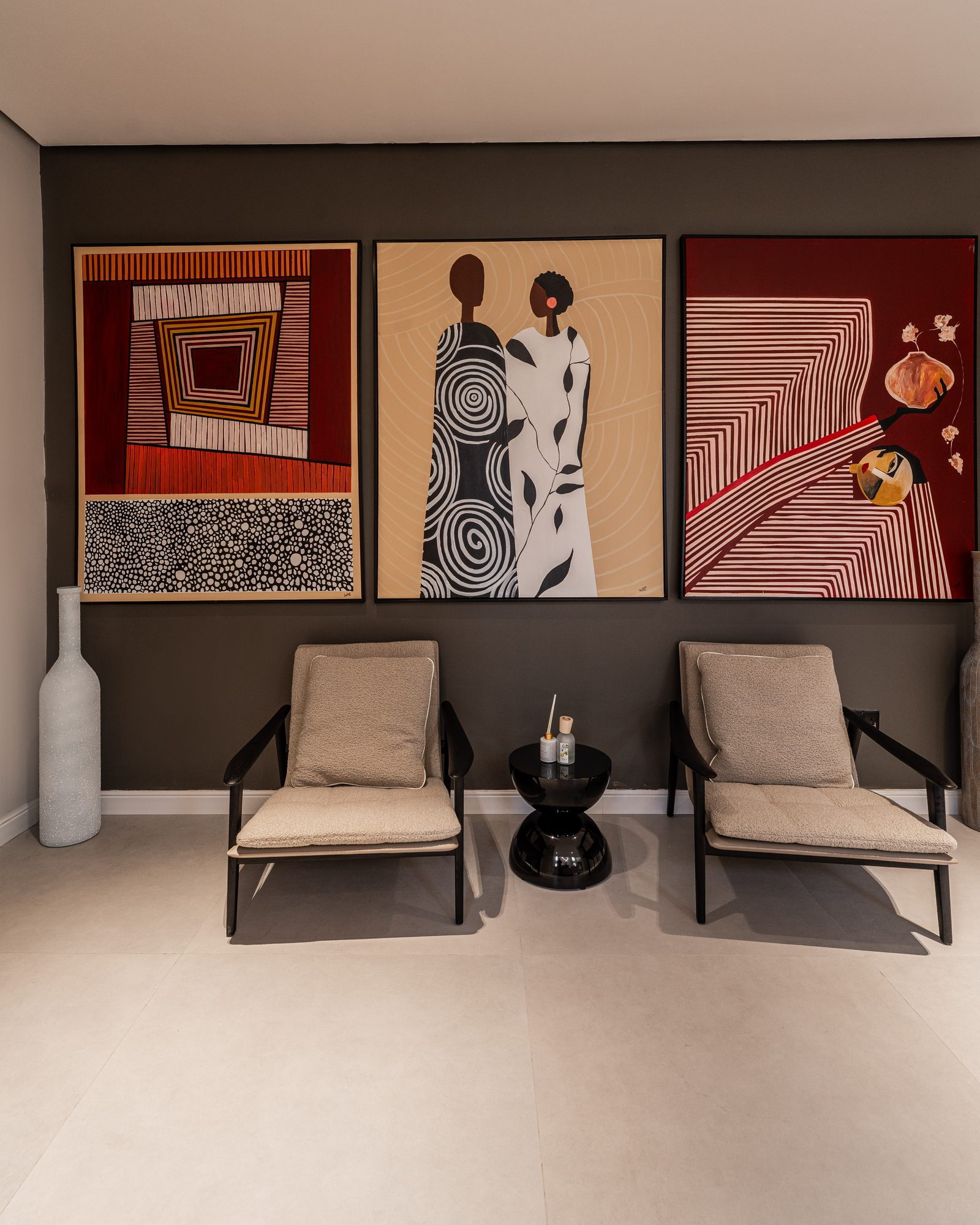 The triptych and two tan armchairs on a charcoal wall