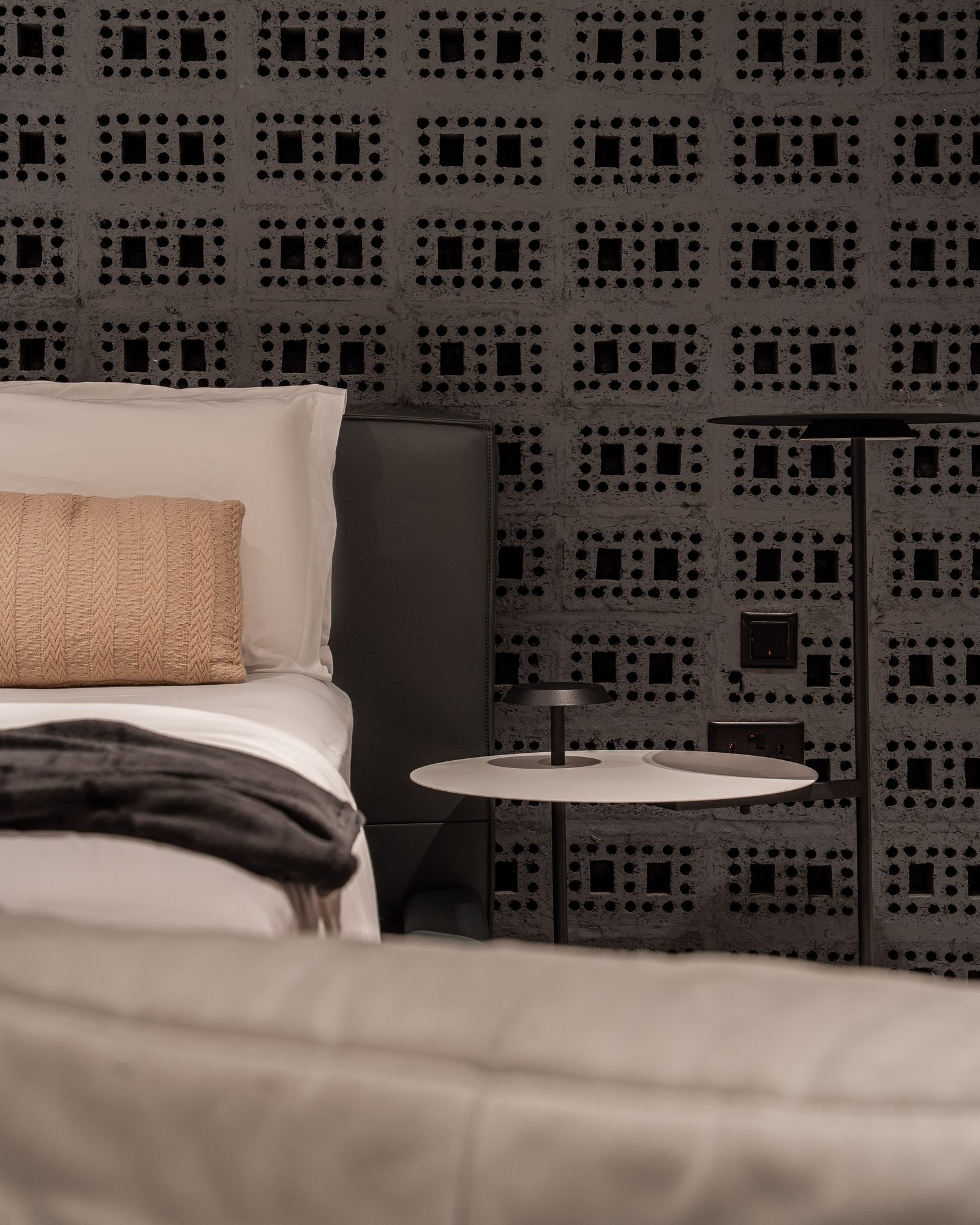 The perforated charcoal screen wall behind the bed, a side table in white marble